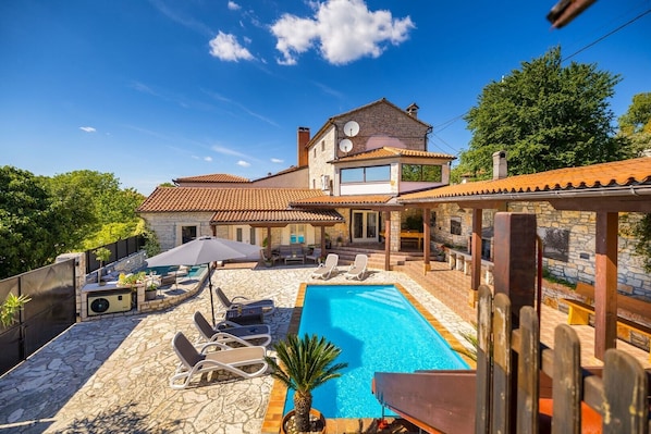 Ein Pool mit LiegestĂŒhlen, eine Steinterrasse und ein Steinhaus mit Ziegeldach.