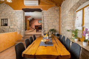 Un comedor con una larga mesa de madera, paredes de piedra y vistas a una escalera que baja a un nivel inferior.