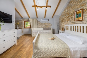 A bedroom with a stone wall, wooden beams, a bed, a dresser, and a TV.