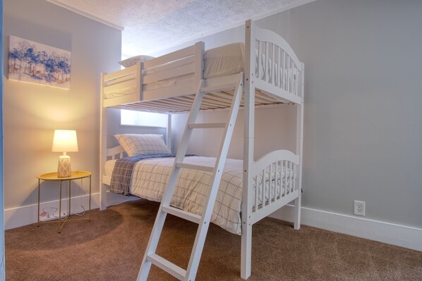A bunk bed with a ladder, a bedside table with a lamp, and a wall with a painting.