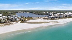 Ett flygbildsbild av ett kustområde med en strand, en flod och ett bostadsområde med hus.