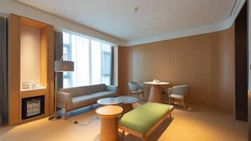 A modern hotel room with a sofa, two round tables, a small coffee table, a TV, and a minibar.