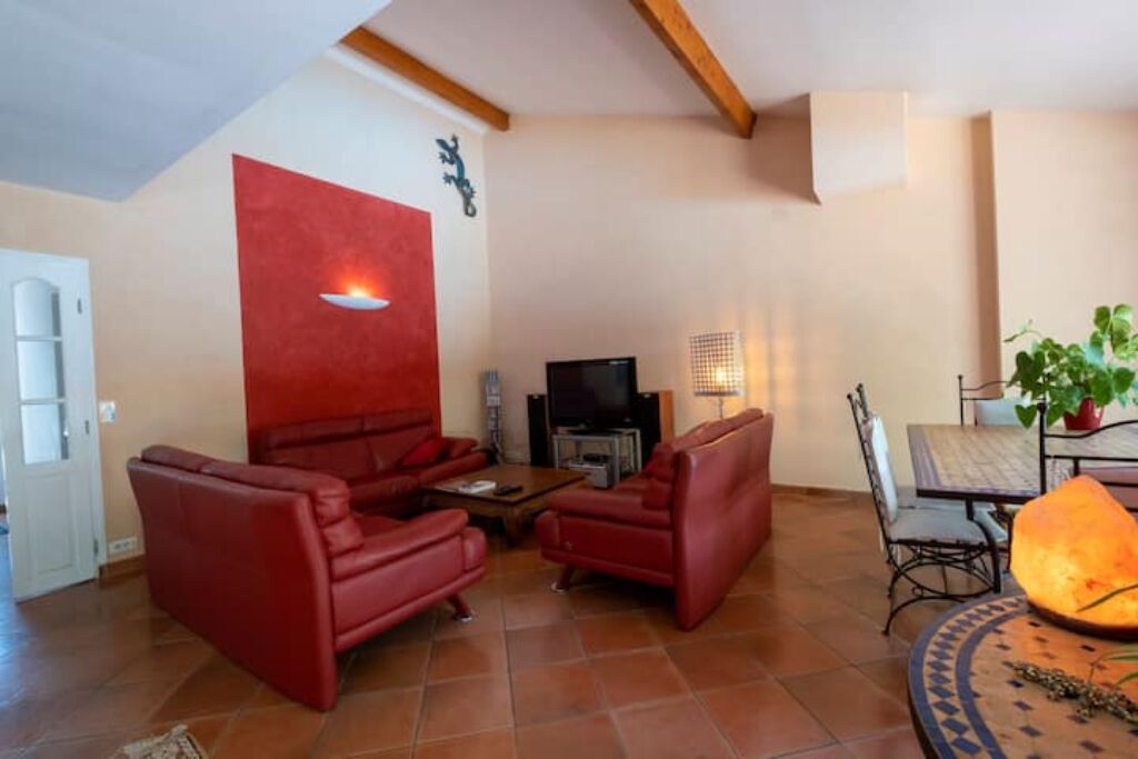 Una sala de estar con sofás de cuero rojo, un televisor y un comedor con mesa y sillas.