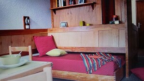 A compact room with a wooden bunk bed, a small table with a bowl and plate, and a shelf with books and picture frames. - SKI IN THE SUN: February 16 to 23, 2025, Serre Chevalier Chantemerle club Maeva (Saint-Chaffrey)