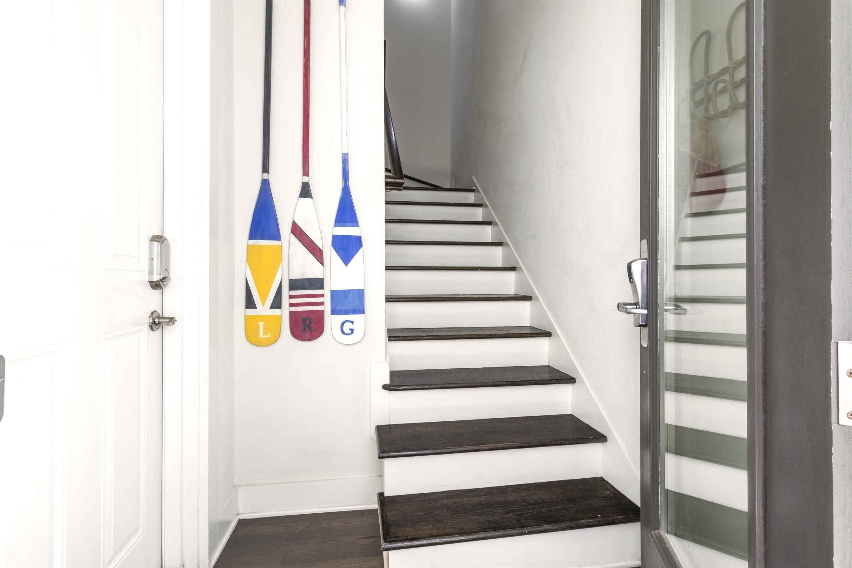 A staircase with white steps and dark wooden handrails, leading to a room with a glass door.