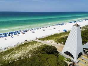 Une plage de sable blanc, des parasols bleus et un grand bâtiment blanc doté d’un toit en forme de flèche.