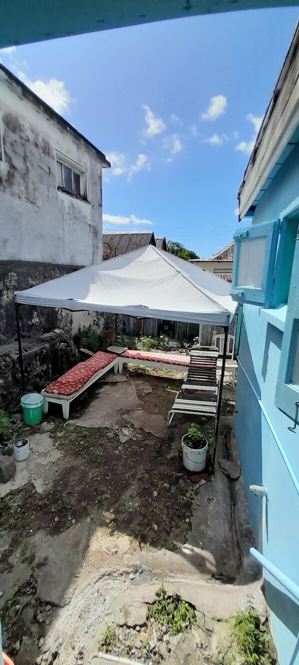 A courtyard with a white tent, two benches, a small garden area, and a blue building. - Bed and Breakfast BNB (Basseterre)