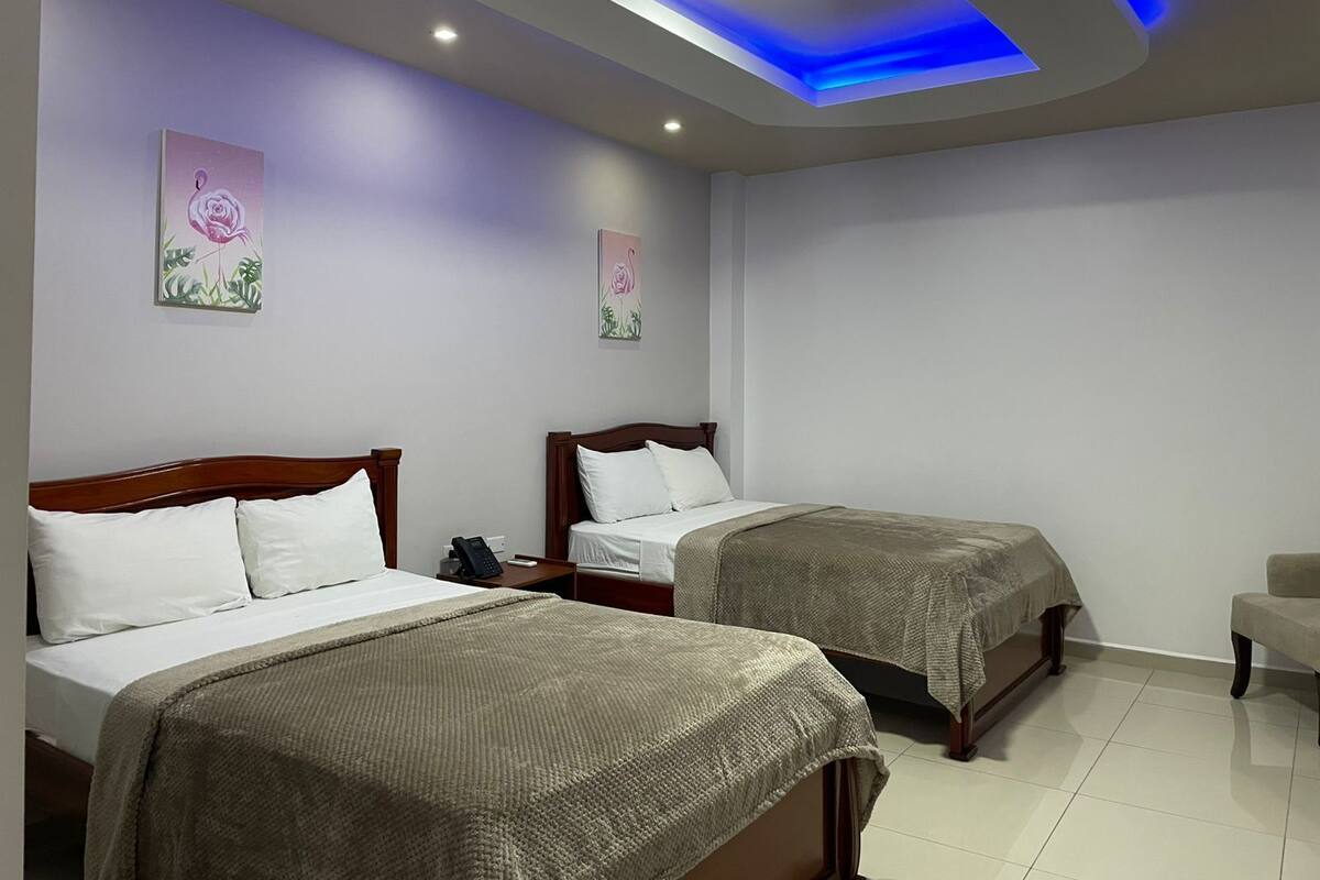A hotel room with two beds, a nightstand, a chair, and a ceiling with blue lighting.