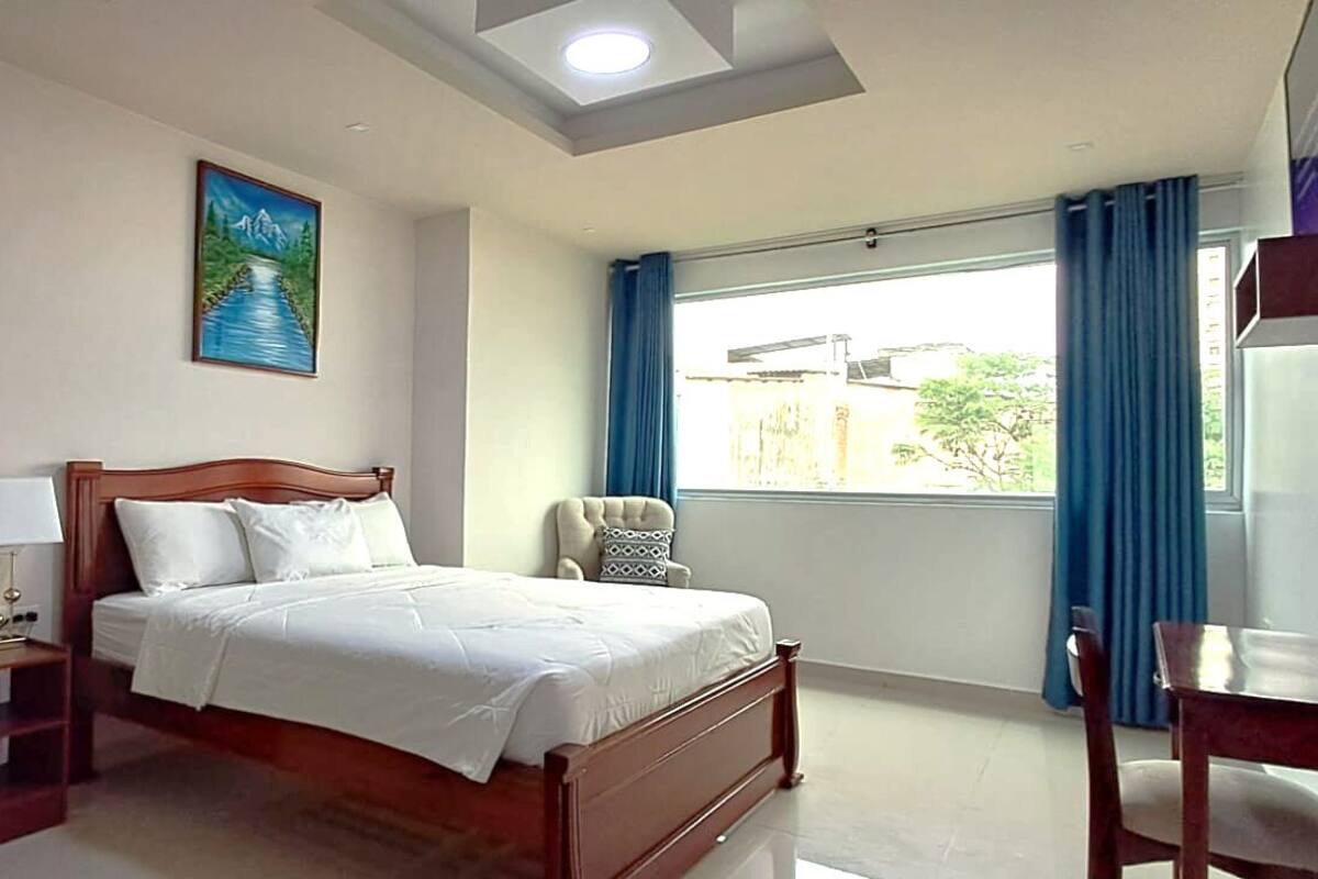A hotel room with a bed, bedside table, lamp, chair, and a window with curtains.