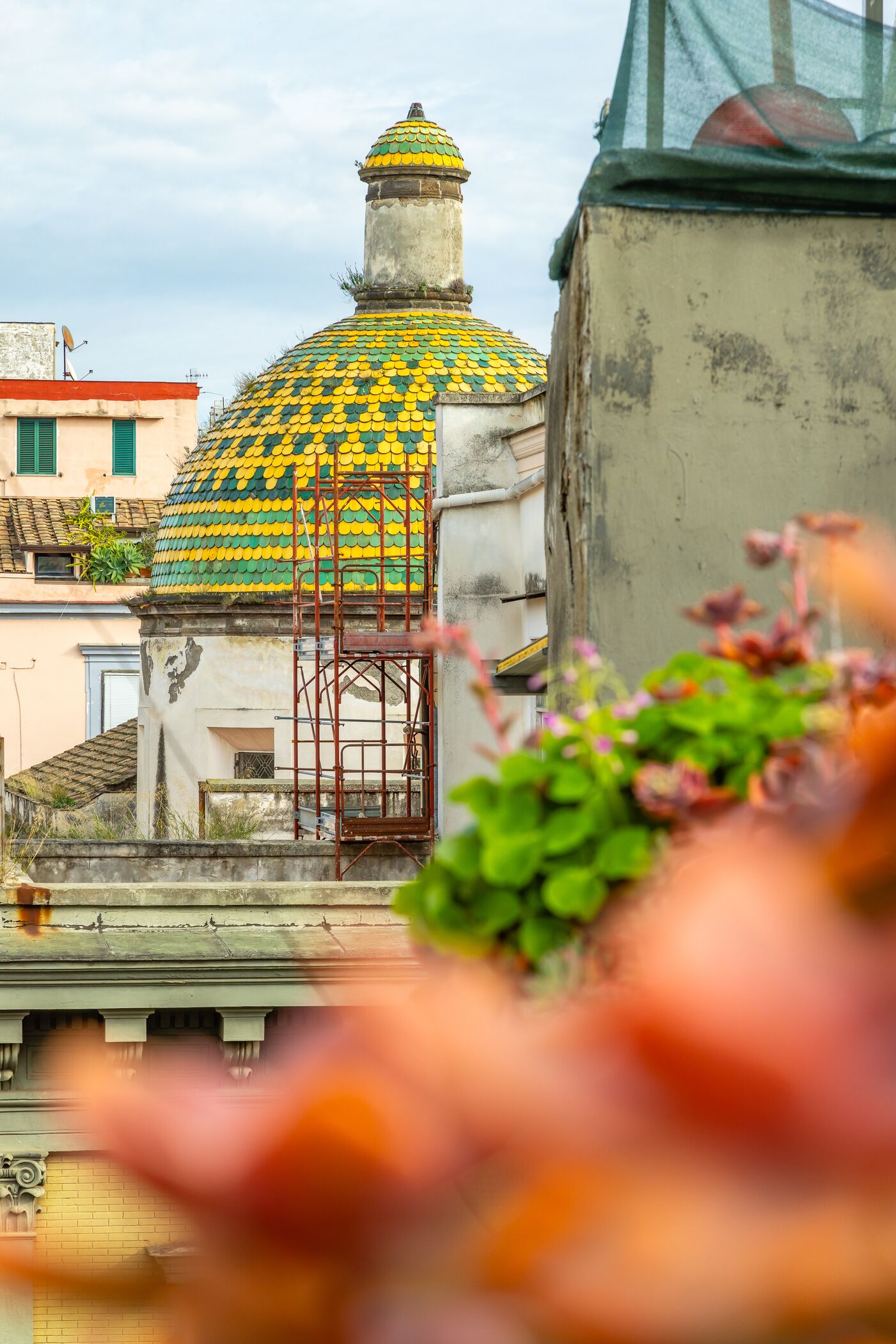 A building with a colorful dome roof, a metal staircase, and a view of surrounding buildings.