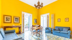 Une pièce lumineuse aux murs jaune vif, comprenant une table à manger, des chaises, un canapé et un fauteuil bleu.