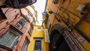 Une rue étroite bordée d’immeubles jaunes et roses, une enseigne indiquant « Casa Hosteno », et des câbles électriques apparents.