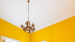 Une pièce aux murs jaunes, avec un sol à motifs bleus, un lustre, un canapé bleu et une table à manger avec des chaises.