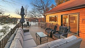 A wooden deck with outdoor seating, overlooking a body of water and a forested area. - Woodhaven on Pleasant Lake |Pleasant Lake |Lakefront |Wraparound Deck |Views |Dock |Kayaks & Boards (East Troy)