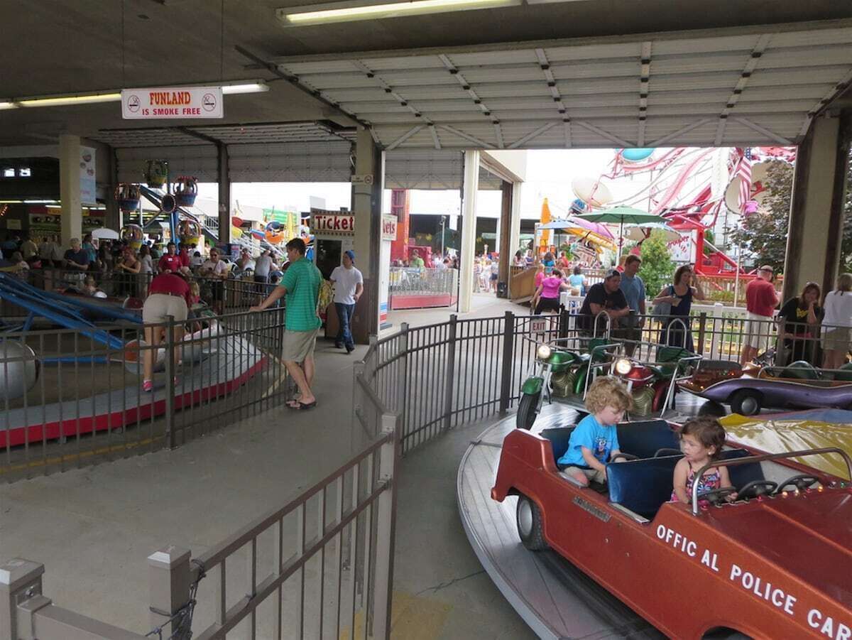 Une zone abritée comprenant des attractions, avec un guichet de vente de billets, une grande roue et une attraction où l’on peut monter dans une voiture de police.