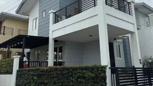 A modern two-story house with a balcony, a covered porch, and a gated entrance. - 2BR Home (corner lot). With Lanai, 100 Mbps Internet and Netflix. (Balanga)