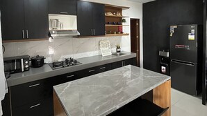 A modern kitchen with dark cabinets, a marble countertop, a built-in oven, and a black refrigerator. - 2BR Home (corner lot). With Lanai, 100 Mbps Internet and Netflix. (Balanga)