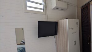 A room with a TV mounted on the wall, a wardrobe, and a window with blinds.
