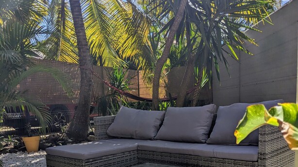 A modern outdoor seating area with a sectional sofa and a small table, surrounded by pebbles and plants.