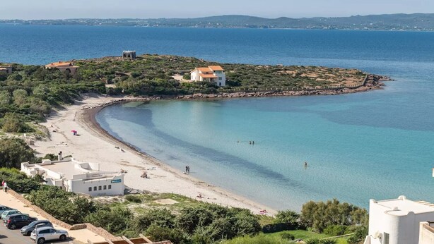 Een kustgezicht met een strand, helderblauw water en gebouwen aan de kust.