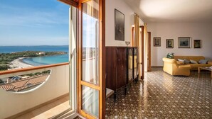 Een balkon met uitzicht op een strand en de oceaan, een houten kast, een gele bank en betegelde vloeren.