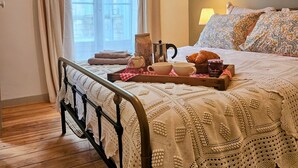 A cozy bedroom with a bed, a wooden floor, a window with sheer curtains, and a tray with breakfast items. - La Forge - Historical Apartment in Sarlat (Sarlat-la-Canéda)