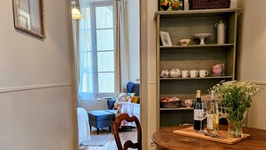 A wooden-floored hallway leading to a dining area with a round table, chairs, and a bookshelf with decorative items. - La Forge - Historical Apartment in Sarlat (Sarlat-la-Canéda)