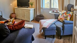 A cozy living room with a sofa, a television, and a window with curtains. - La Forge - Historical Apartment in Sarlat (Sarlat-la-Canéda)