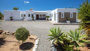 Un edificio moderno de color blanco con fachada de piedra, camino de grava y plantas en macetas.