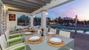 Comedor con mesa lista para cuatro, piscina exterior y sillones de descanso.