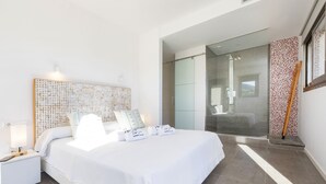 A modern bedroom with a large bed, a bedside table with a lamp, and a glass shower area.