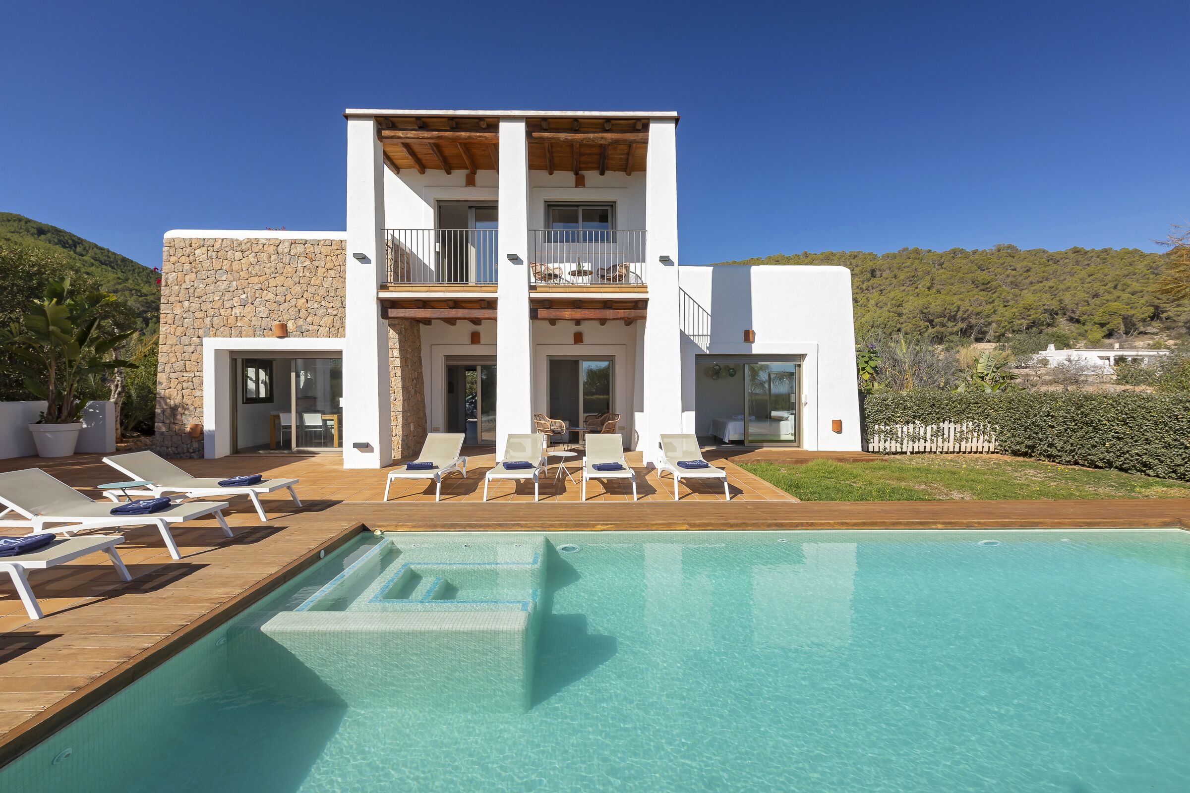 A modern two-story building with a pool, lounge chairs, and a view of the surrounding landscape.