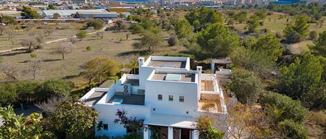 Una moderna casa bianca con tetto piatto, immersa nel verde e con vista sulla città costiera.