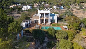 A modern villa with a pool, surrounded by lush greenery and hills.