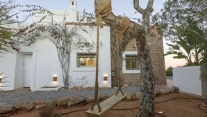 A rustic outdoor area with a wooden swing, a stone wall, and a white building with windows. - Villa in Ibiza Town Sleeps 12 (Ibiza)