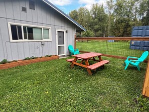 A backyard with a wooden picnic table and two chairs, a wooden deck, and a fenced area.