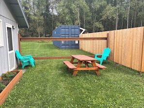 Un jardin avec une clôture en bois, une table de pique-nique et deux chaises turquoise.