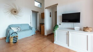 A living room with a blue sofa, a wicker basket, a white cabinet, and a flat-screen TV mounted on the wall.