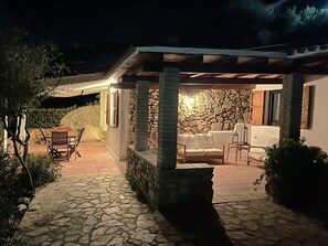 A stone-floored patio with outdoor furniture, a stone wall, and a covered seating area. - DOMUS SUN: Sea and Sardinian Relaxation! (VILLASIMIUS CAMPULONGU)
