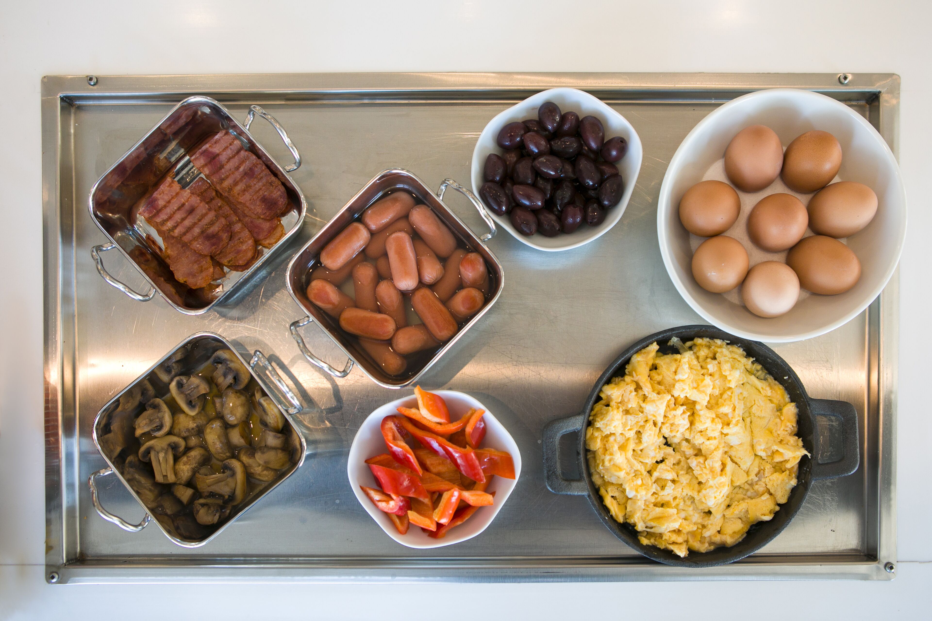 Una bandeja con diversos alimentos, entre ellos salchichas, frijoles, huevos, champiñones y pimientos.