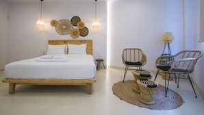 A bedroom with a large bed, two wall-mounted lights, a small stool, and wicker chairs. - White Corner (Thessaloniki)
