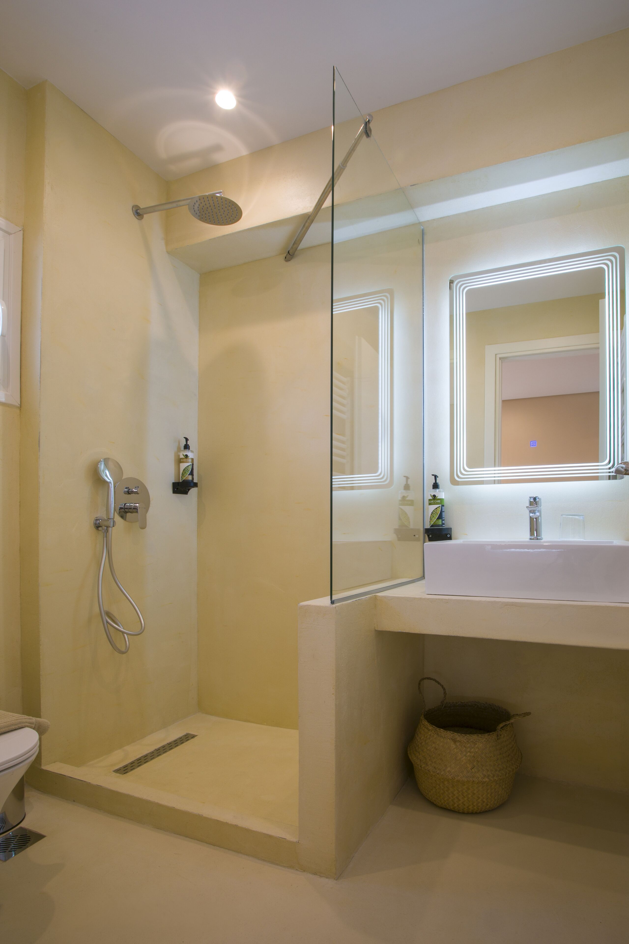 A modern bathroom with a glass-enclosed shower, a large mirror with integrated lighting, and a white sink.