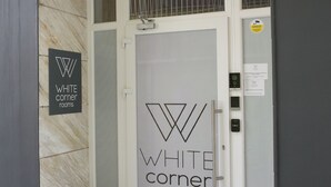 A hotel entrance with a glass door, a sign reading "WHITE corner rooms," and a metal handle. - White Corner (Thessaloniki)