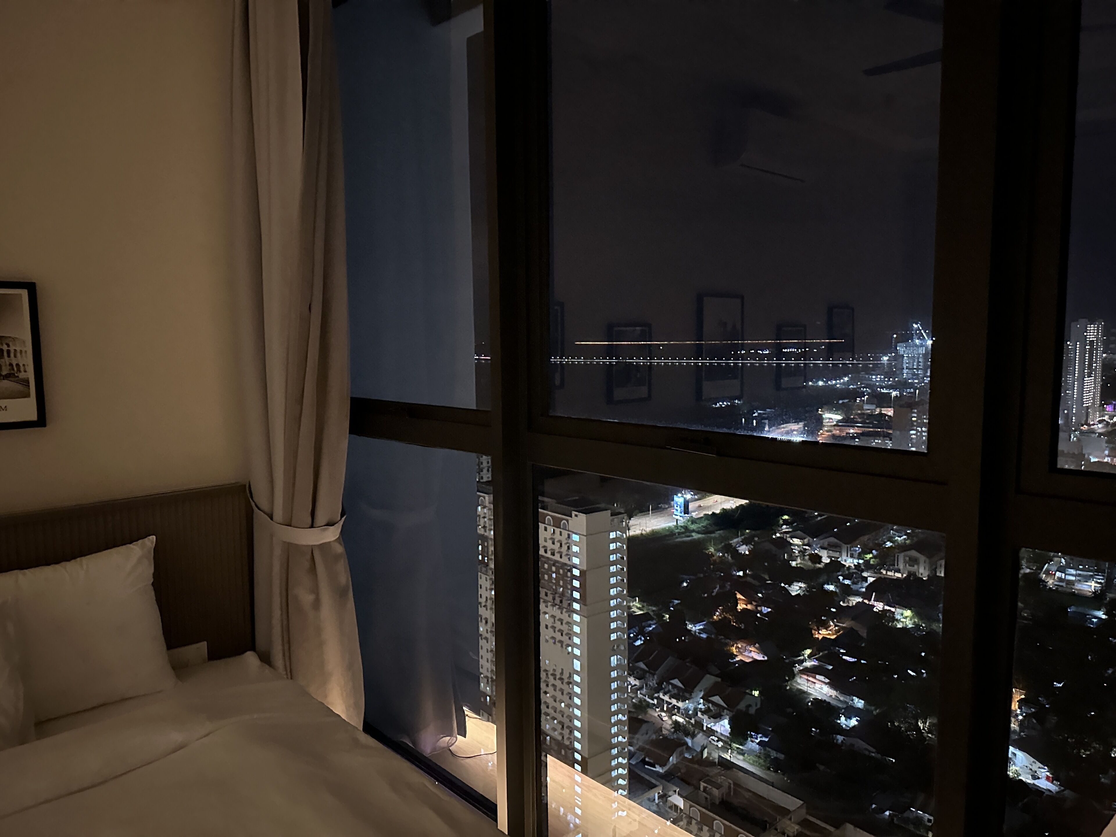 Hotellihuone, jossa on suuri ikkuna, josta avautuu näkymä kaupunkiin yöllä.