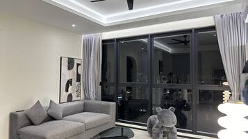 Un salon moderne avec un canapé gris, une table basse en verre et une grande fenêtre agrémentée de rideaux.