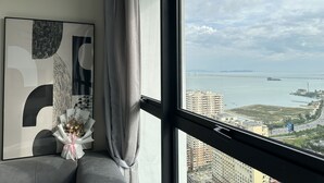 A modern room with a large window, a framed abstract artwork, and a bouquet of flowers on a gray sofa.