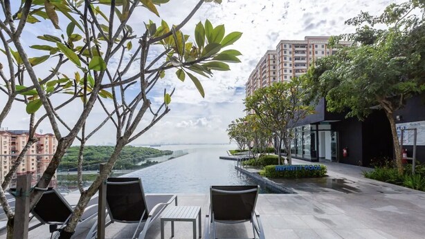 A rooftop terrace with a view of a river, outdoor seating, and modern buildings in the background.