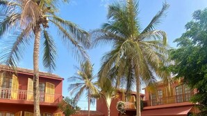A hotel with a pool, palm trees, and a red building facade. - Les Goréennes Suites (Mbour)