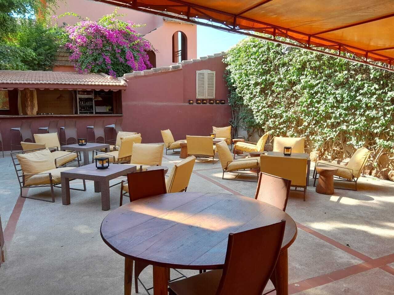 Une terrasse extérieure dotée de plusieurs espaces de détente, comprenant des tables rondes et des chaises rembourrées, le tout abrité sous une grande auge.