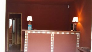 A reception area with a tiled floor, a reception desk, two wall-mounted lamps, and a ceiling light fixture. - Les Goréennes Suites (Mbour)